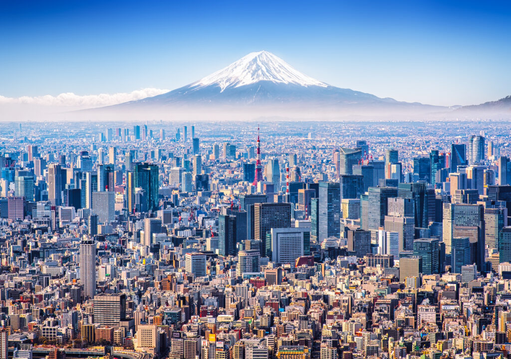 Een weidse luchtfoto van de skyline van Tokio met de rood-witte Tokyo Tower, met op de achtergrond de met sneeuw bedekte top van Mount Fuji.