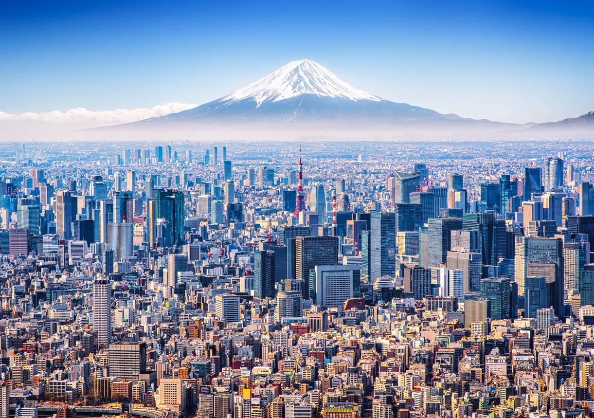 Een weidse luchtfoto van de skyline van Tokio met de rood-witte Tokyo Tower, met op de achtergrond de met sneeuw bedekte top van Mount Fuji.