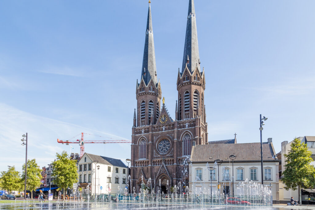Een zonnig beeld van de Sint-Jozefkerk (Heuvelse kerk) aan het bekende plein de Heuvel in Tilburg, met de fonteintjes op de voorgrond.