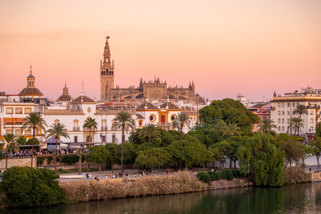 Uitzicht vanaf de overkant van de rivier Guadalquivir op de grote kathedraal van Sevilla tijdens een zachte, roze zonsondergang.