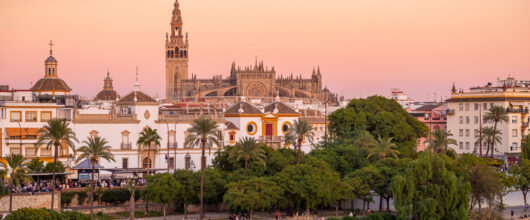 Uitzicht vanaf de overkant van de rivier Guadalquivir op de grote kathedraal van Sevilla tijdens een zachte, roze zonsondergang.