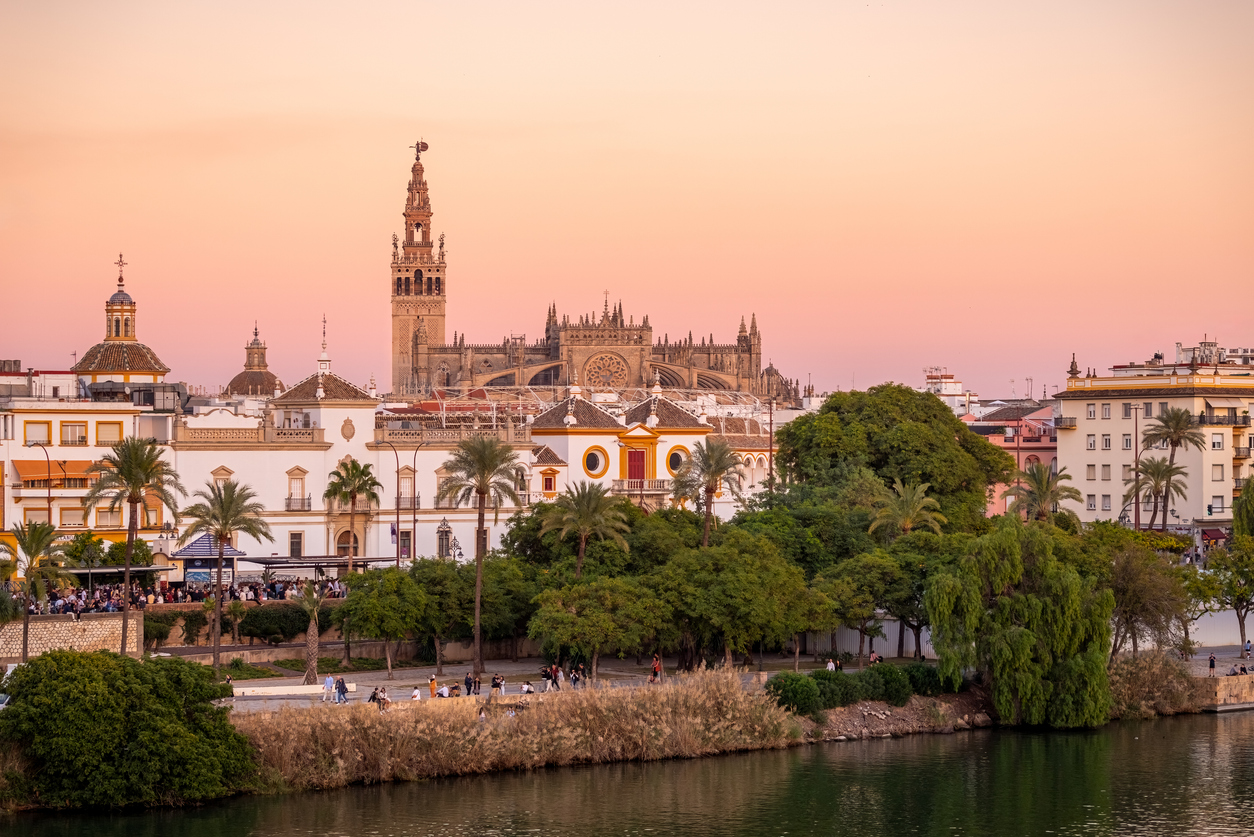 Uitzicht vanaf de overkant van de rivier Guadalquivir op de grote kathedraal van Sevilla tijdens een zachte, roze zonsondergang.