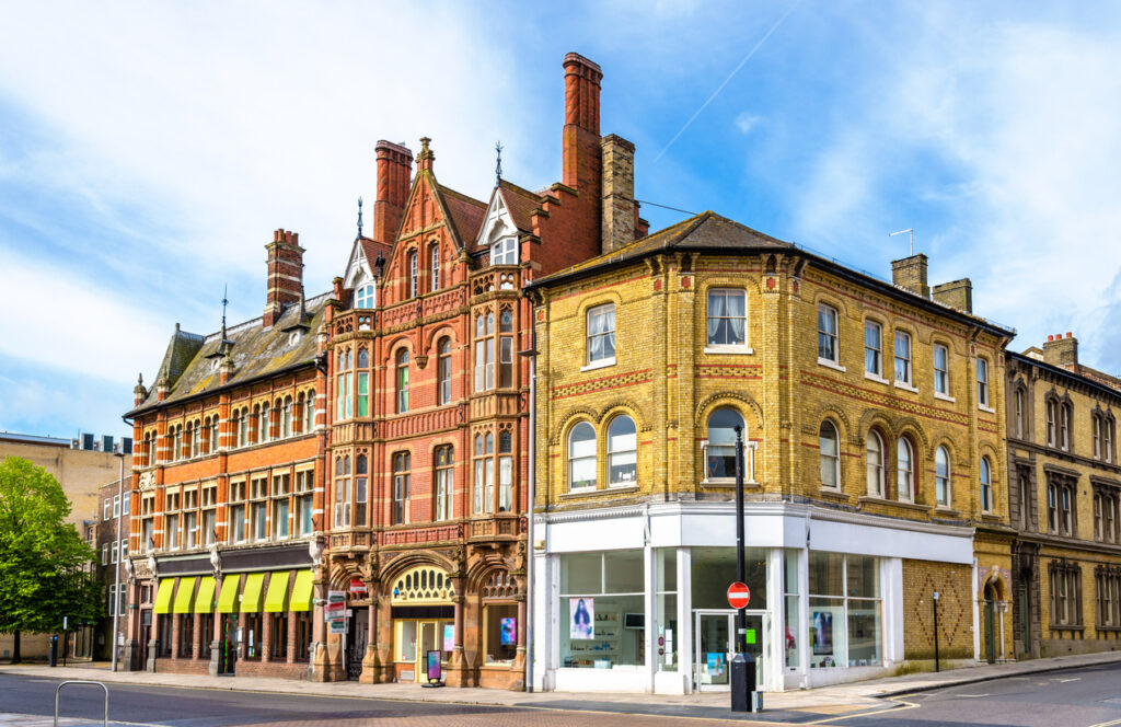 Straatbeeld van historische architectuur in Southampton met een statig roodbruin bakstenen gebouw met sierlijke bogen en ornamenten, geflankeerd door een geel bakstenen hoekpand onder een blauwe lucht met lichte wolken.