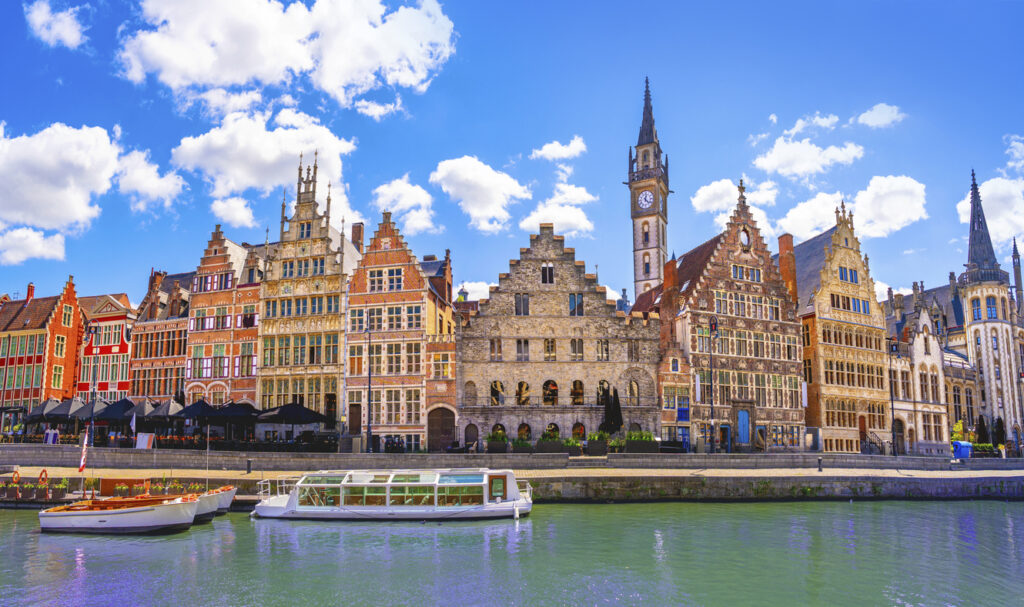 Kleurrijke historische gildehuizen aan de Graslei in Gent, weerspiegeld in het water onder een blauwe lucht met wolken.