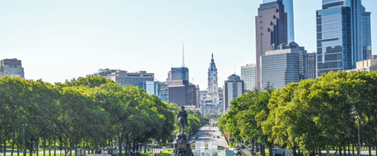 Een stadsgezicht in vogelvlucht op de Benjamin Franklin Parkway in Philadelphia, met het ruiterstandbeeld van het Washington Monument omringd door bomen en wolkenkrabbers.
