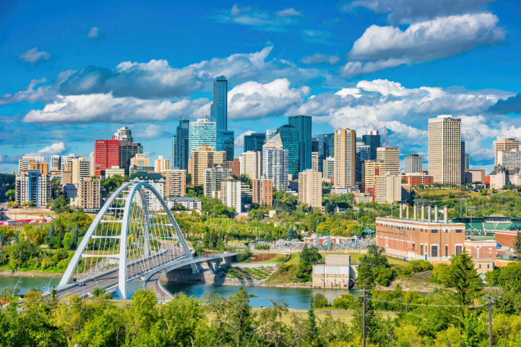 Een zonnig stadsgezicht op de skyline van Edmonton met moderne wolkenkrabbers en de opvallende witte Walterdale-boogbrug over de rivier.