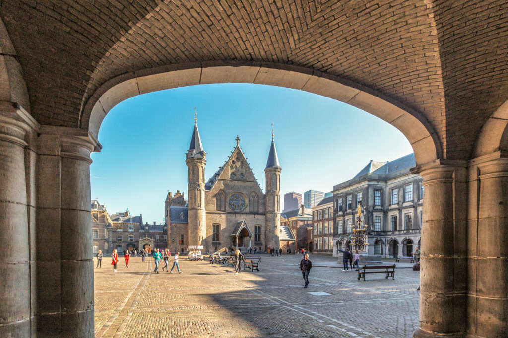 Doorkijkje door een stenen boogpoort naar de Ridderzaal op het Binnenhof in Den Haag.