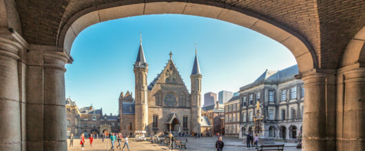 Doorkijkje door een stenen boogpoort naar de Ridderzaal op het Binnenhof in Den Haag.