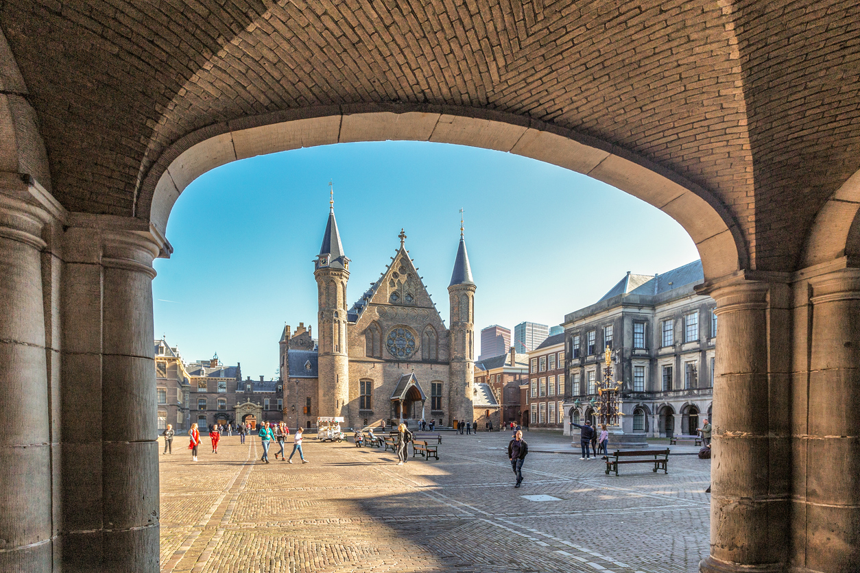 Doorkijkje door een stenen boogpoort naar de Ridderzaal op het Binnenhof in Den Haag.